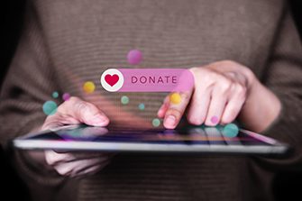 Hand interacting with a tablet with a pink donate button floating over the top.