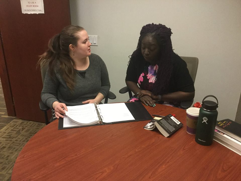 Two women talking over a piece of writing in a binder.