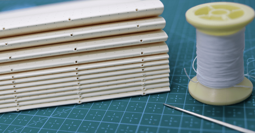 Book binding materials: thread, needle, and paper signatures.