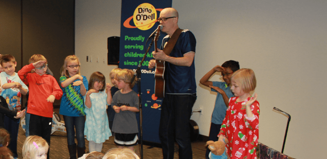 Dino O'Dell playing guitar and dancing with children.
