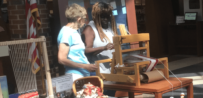 Weaver from the Iowa City Area Craft Guild showing a woman her loom.