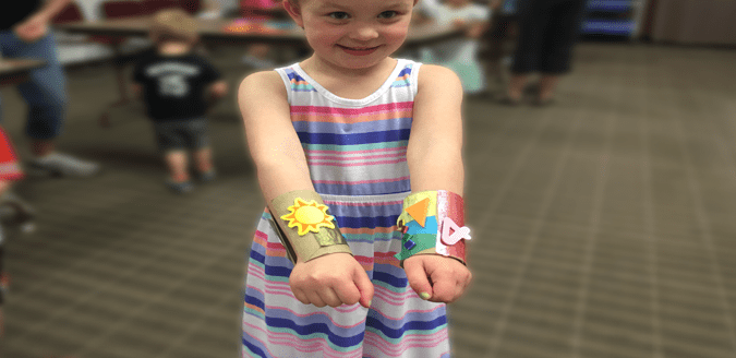 Child showing off their superhero cuffs make out of decoratead toilet paper rolls.