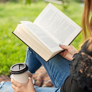 A woman reading a book outside with a drink